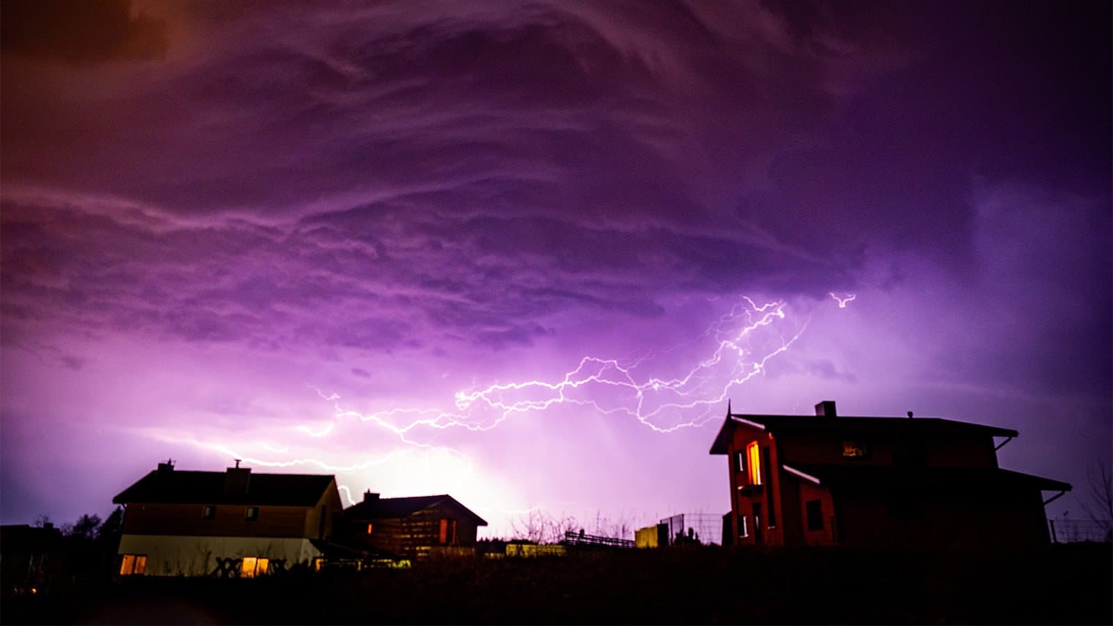 Valley with houses on it under a cloudy sky during storm in the night